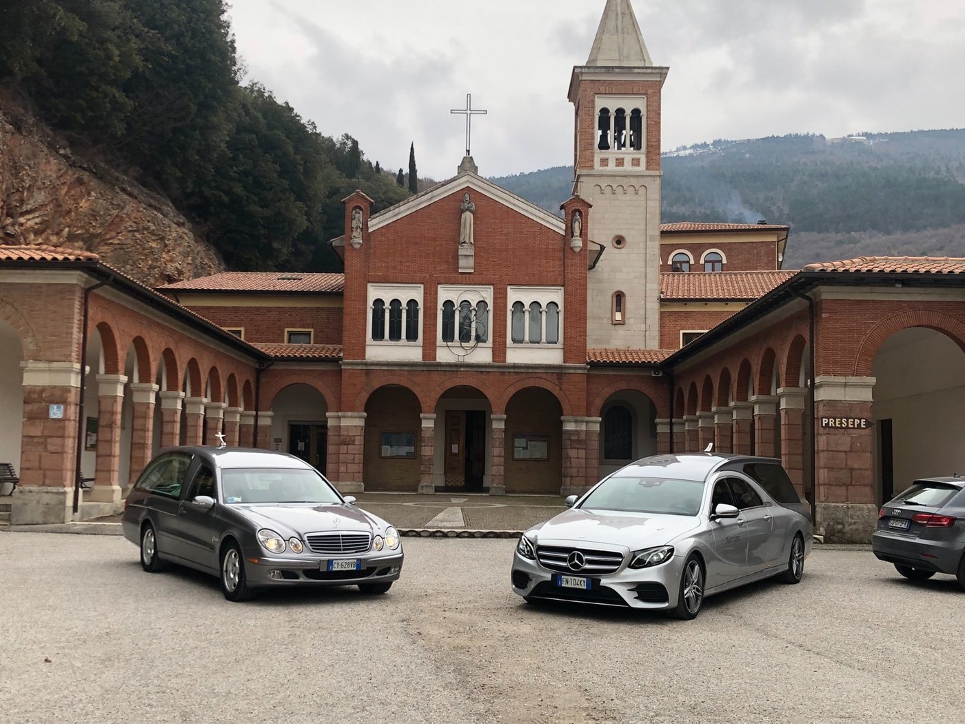 Due auto funebri Mercedes Morroni davanti a una chiesa in mattoni rossi con campanile e portici ad archi